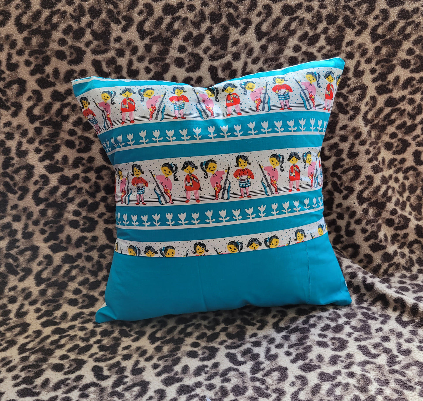 Home-made vintage-style nursery cushion cover depicting pony-tailed girls playing musical instruments, with contrast white reverse