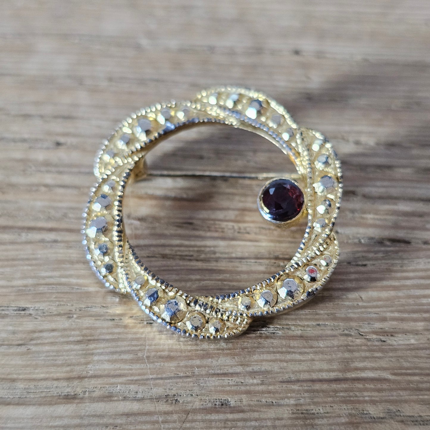 1980s gold-tone faux marcasite circle brooch with garnet rhinestone
