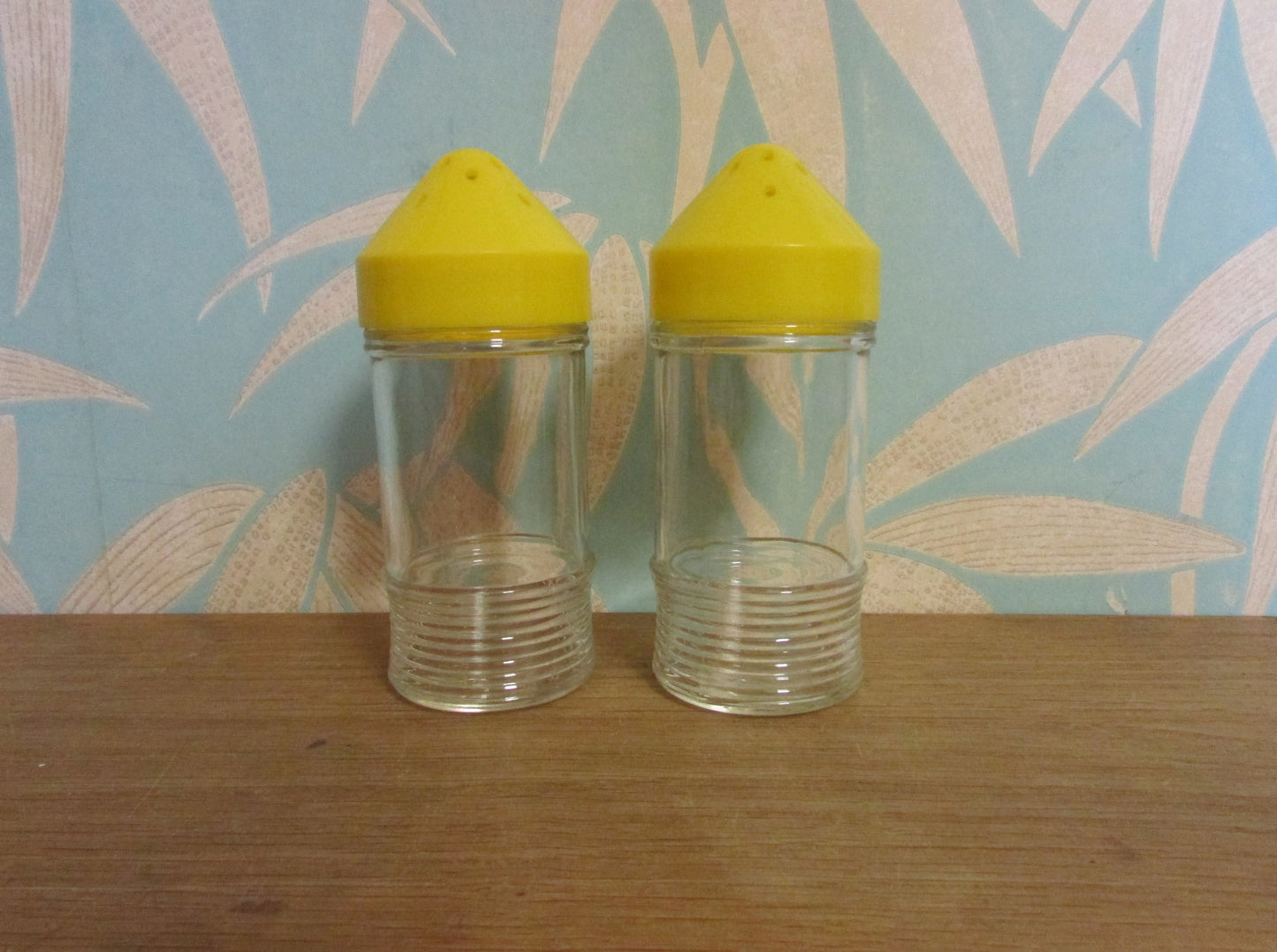 Pair of 1960s glass sugar pourers with yellow plastic lids