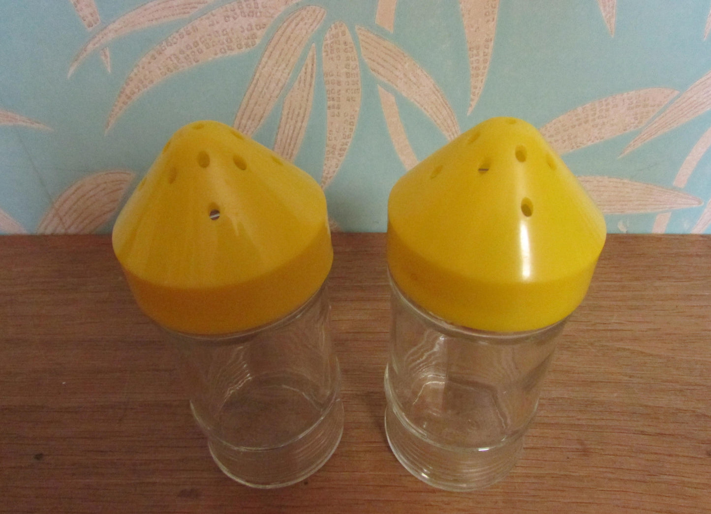 Pair of 1960s glass sugar pourers with yellow plastic lids