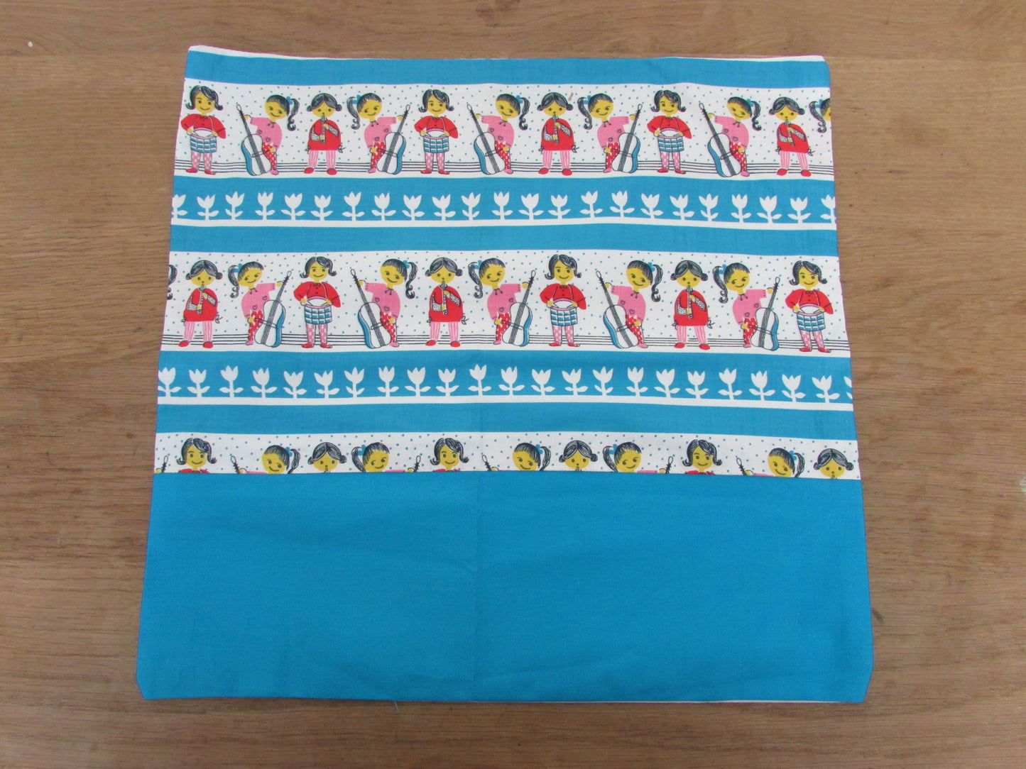 Home-made vintage-style nursery cushion cover depicting pony-tailed girls playing musical instruments, with contrast white reverse