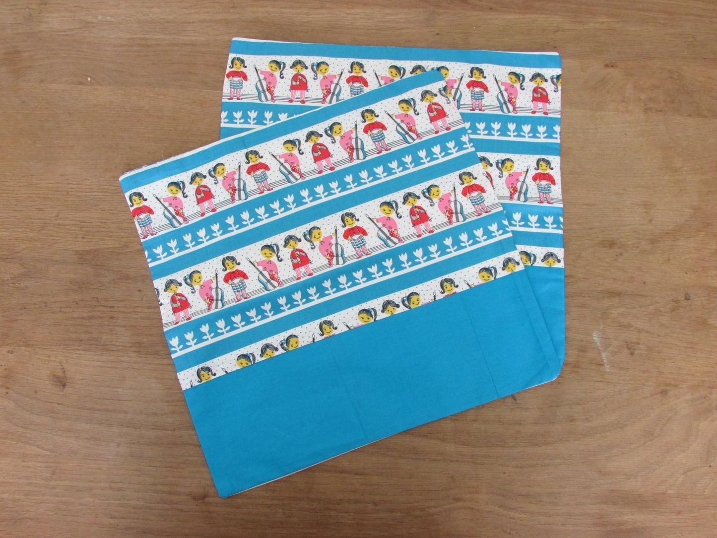 Home-made vintage-style nursery cushion cover depicting pony-tailed girls playing musical instruments, with contrast white reverse