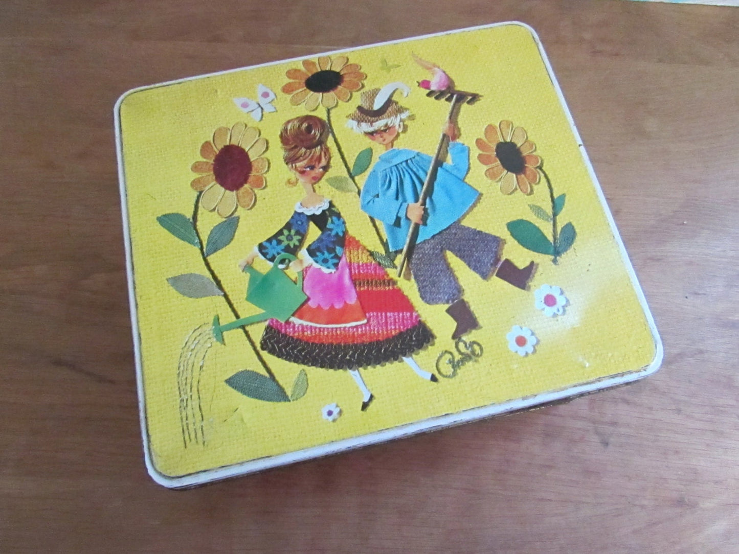 Fun collectable 1960s/70s yellow & orange floral patterned tin, kitsch couple on lid watering sunflowers